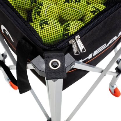 Close up of trolley with black bag and black mesh top for tennis balls. Orange line on the side of the bag with HEAD in white writing above.