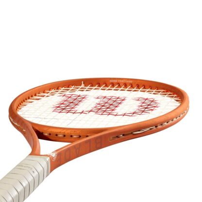Side throat view of Throat view of orange tennis racquet with grey grip and white strings with red "W" for Wilson. White Roland Garros logo at the bottom of the throat. Wilson Blade 98 18x20 v8.0 Roland Garros Edition. Wilson in orange writing on the side of the beam.