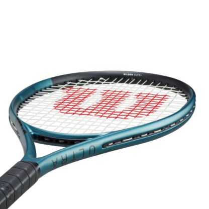 Side throat view of beam of blue matte tennis racquet with black top, white strings with red logo and black grip. Wilson Ultra 26 v4.0. Ultra in black writing on the side.