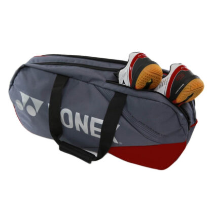 Rectangular greyish pearl/silver grey and red racquet bag from Yonex. Yonex in silver writing with silver Yonex logo. Shoes being put in seperate compartment for shoes.