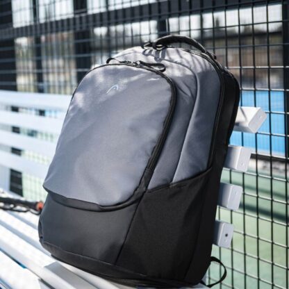 Photo of Black and grey backpack from HEAD on a bench at a court. With small purple HEAD logo on the front. Adjustable shoulder straps in grey. Multiple compartments.